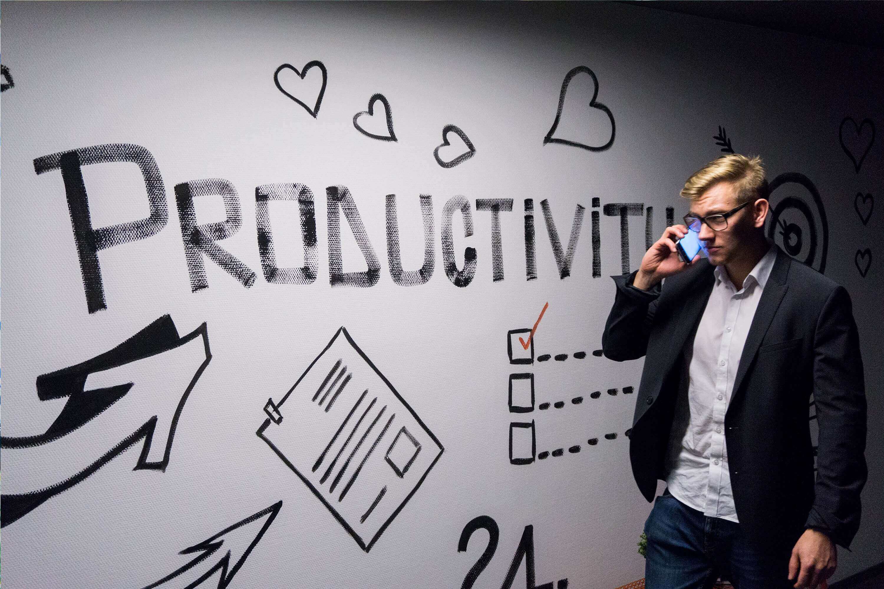 Man on phone in front of white board with "Productivity" written on it