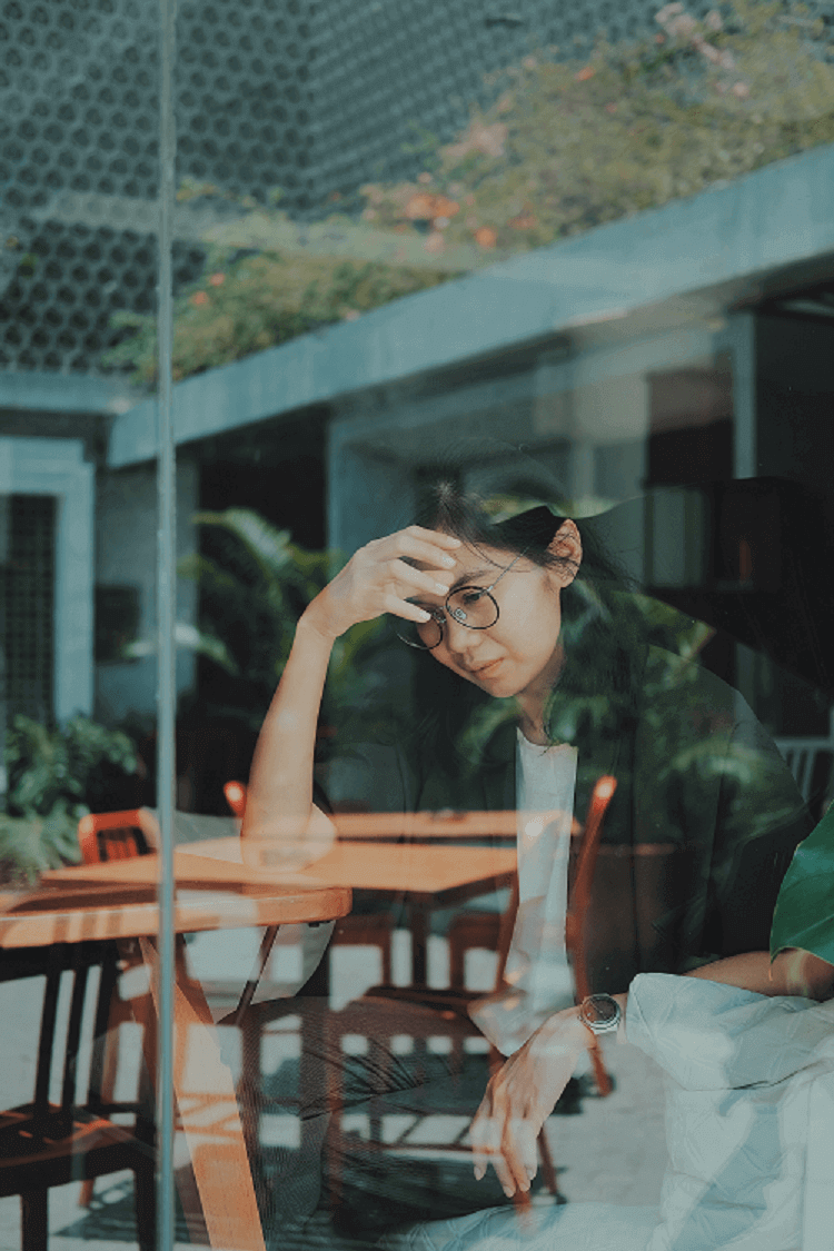Asian woman sitting at table with head down and sad expression